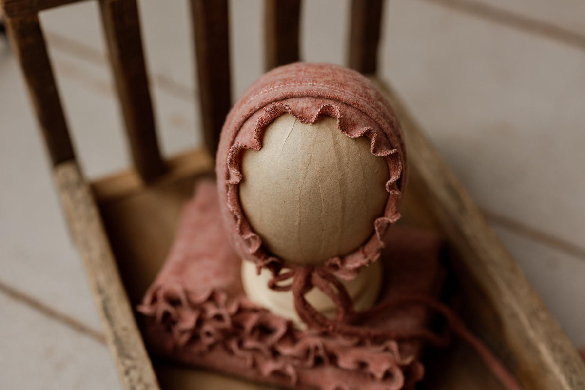 Primrose floral newborn photography set featuring a textured pink ruffle wrap and matching bonnet on a wooden prop.