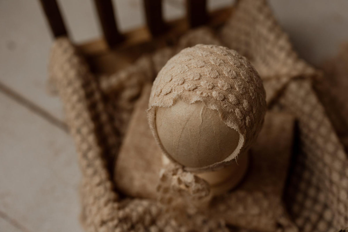 Creamy toffee newborn photography wrap with a soft, raised dot texture and matching bonnet on a wooden prop bed.