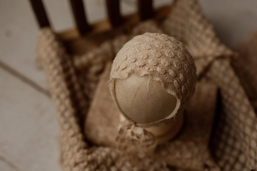 Creamy toffee newborn photography wrap with a soft, raised dot texture and matching bonnet on a wooden prop bed.