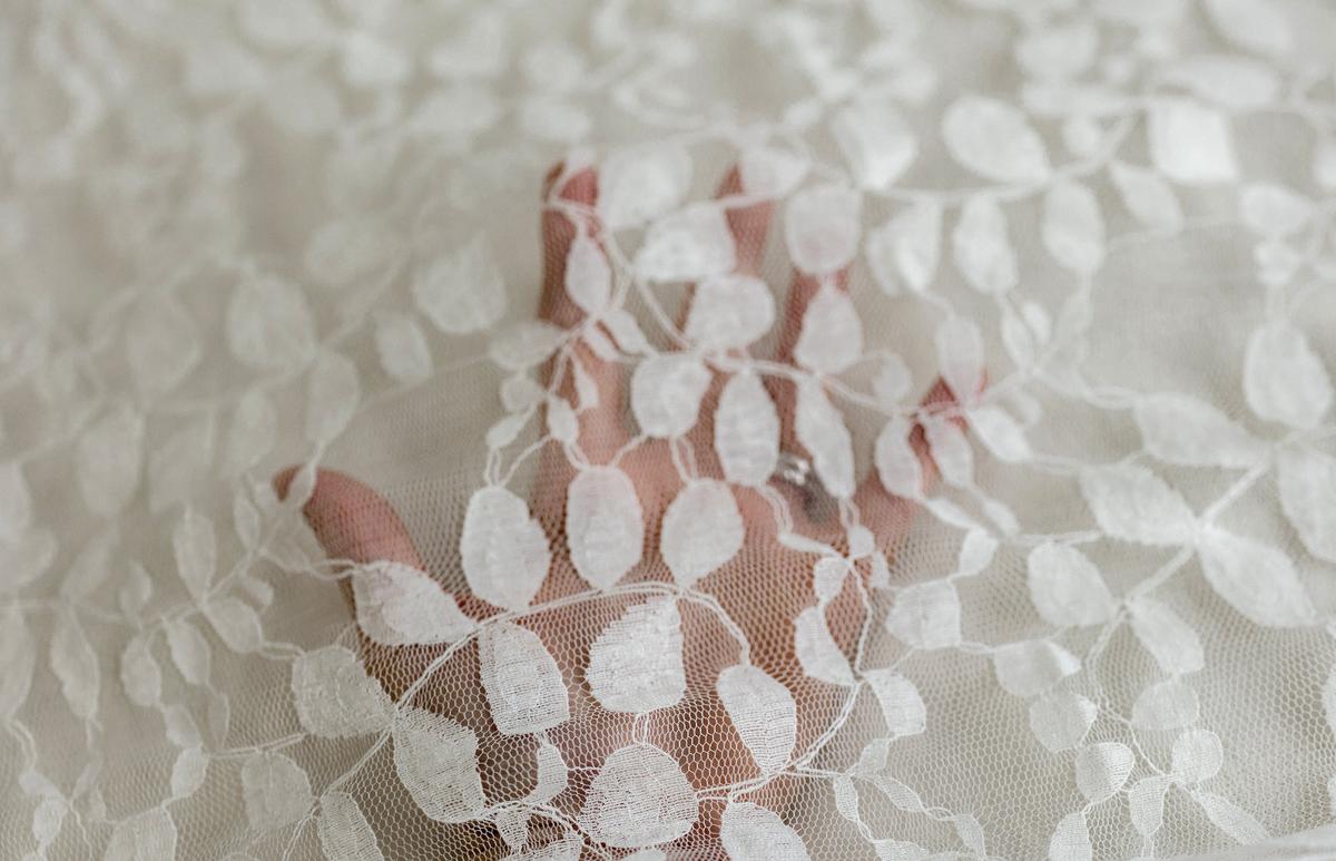 Close-up of sheer ivory lace newborn photography layering fabric with delicate embroidered leaves shown over a hand.