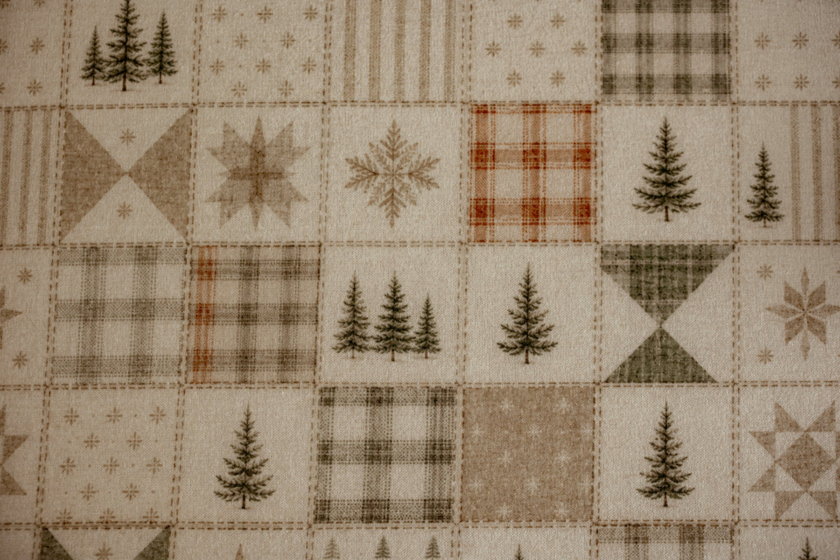 A close-up of a quilted fabric featuring a patchwork design with winter motifs, including pine trees, snowflakes, plaid patterns, and geometric shapes in beige, brown, and muted orange.