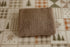 A folded brown ribbed knit newborn photography wrap is placed on a patterned fabric surface with plaid and tree motifs.