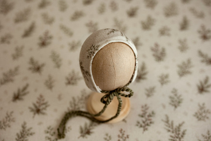 Mantle Garland newborn photography bonnet featuring delicate evergreen branches on cream fabric with coordinating olive green ties.
