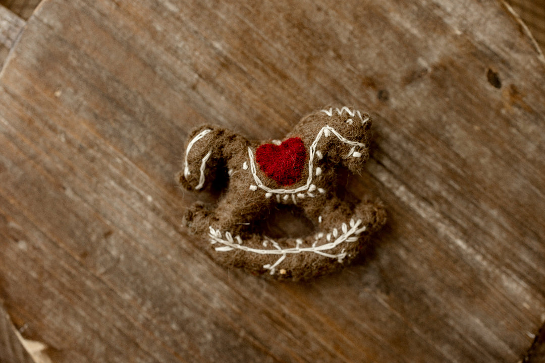 Vintage-inspired brown felted rocking horse newborn photography lovie with cream embroidered details and a red heart accent.