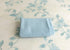 Folded blue ribbed newborn wrap resting on ivory fabric with a vintage watercolor blue floral vine print.
