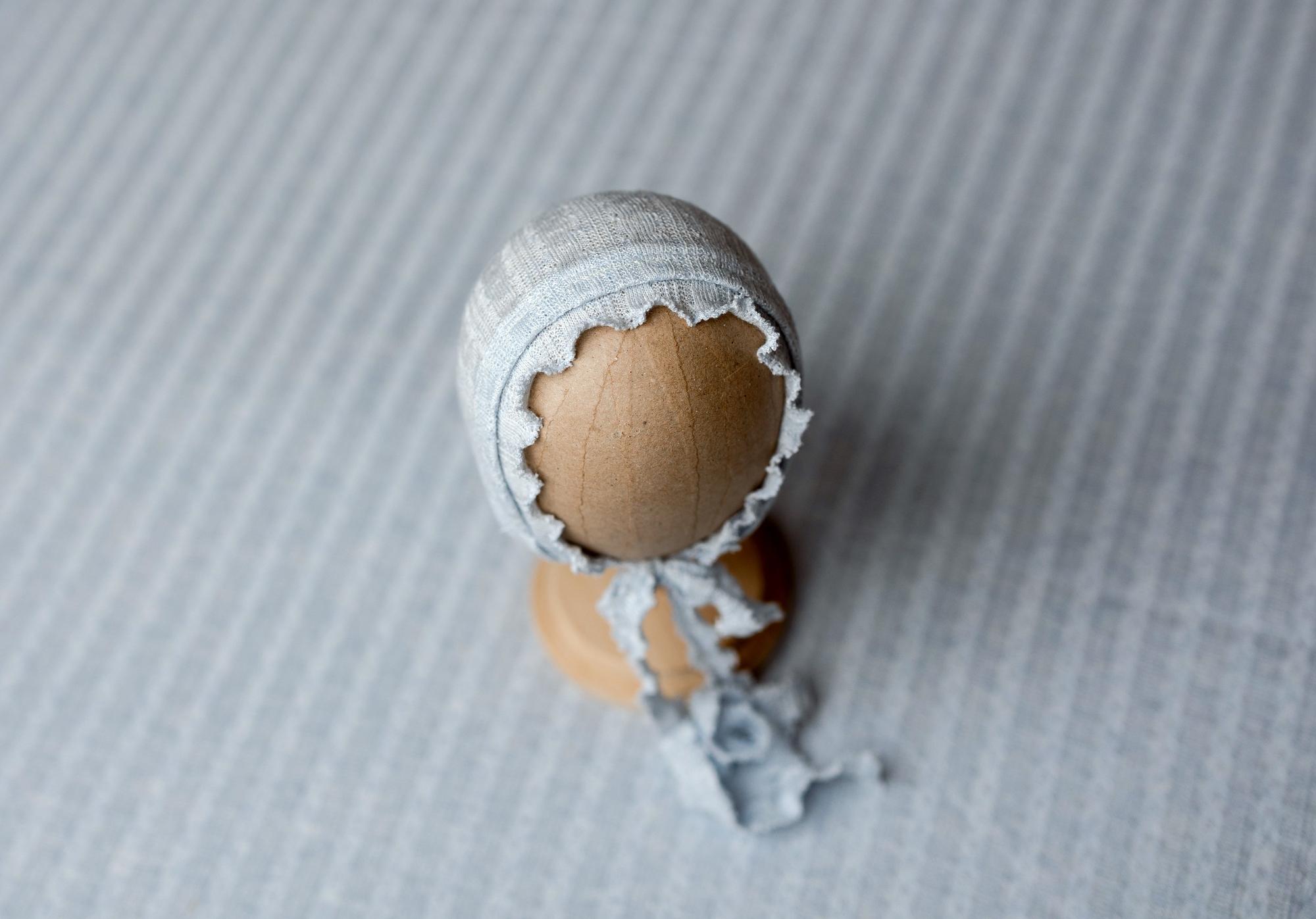 Sky blue newborn photography bonnet made of textured fabric with a delicate ruffled edge and matching tie strings.
