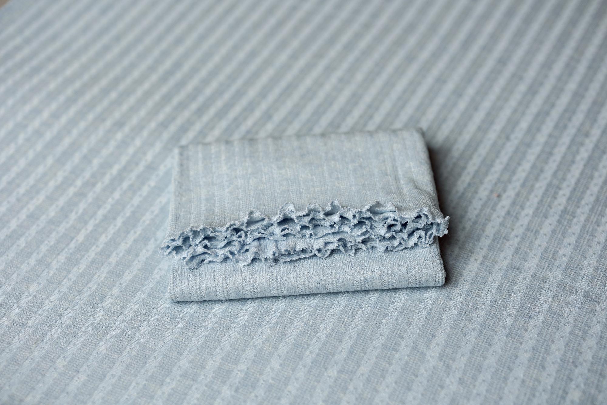 Folded sky blue newborn photography wrap with delicate ruffled edges and a subtle vertical striped texture.
