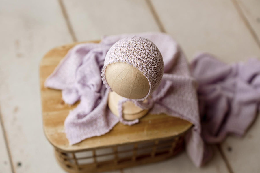 Soft amethyst purple open-knit newborn photography wrap and matching bonnet set draped over a wooden prop.