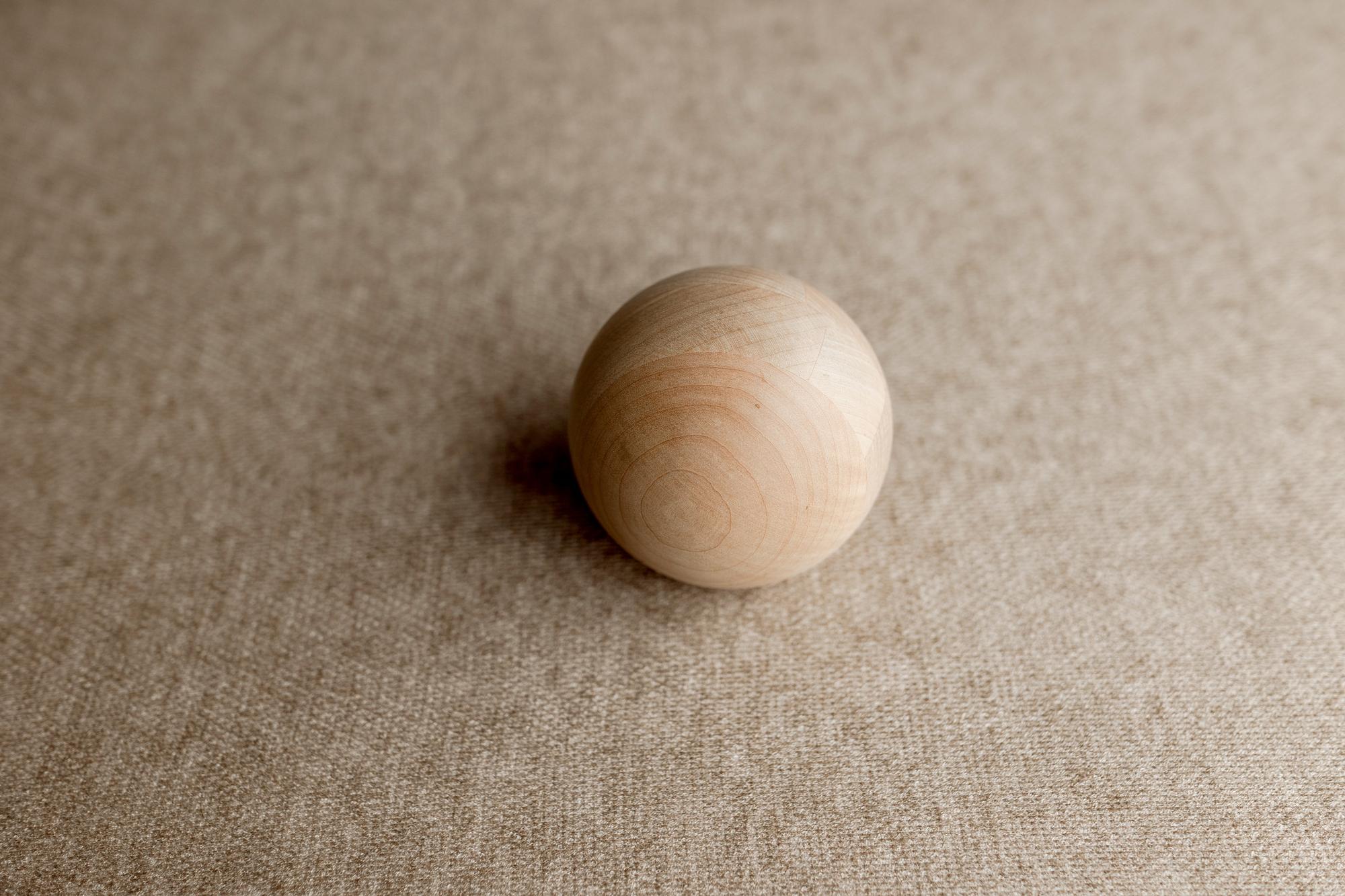Smooth wooden sphere resting on a textured, light brown Charlie Brown posing fabric backdrop.