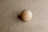 Smooth wooden sphere resting on a textured, light brown Charlie Brown posing fabric backdrop.