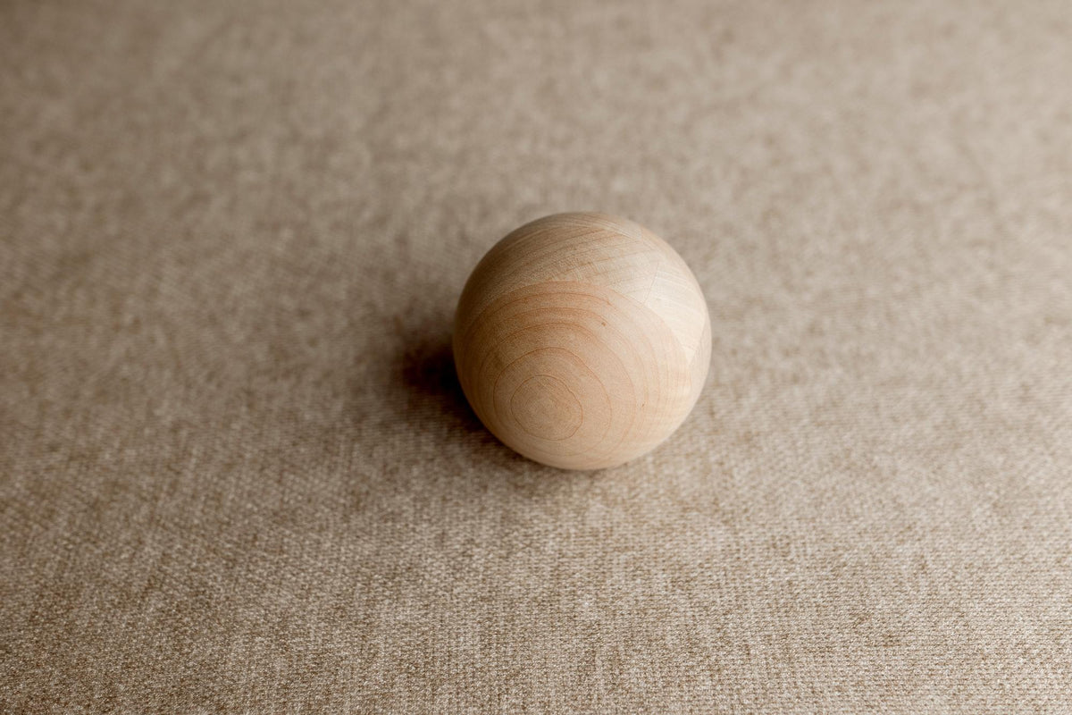 Smooth wooden sphere resting on a textured, light brown Charlie Brown posing fabric backdrop.