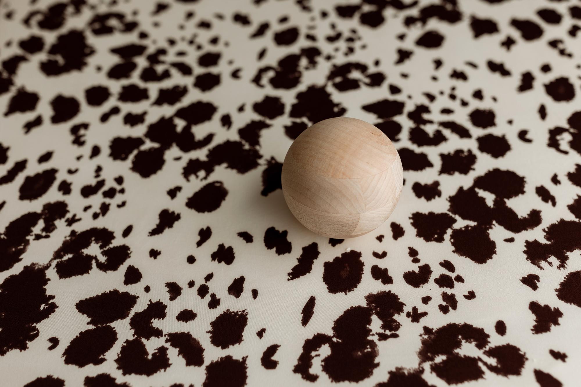 Frontier Days posing fabric with a cream and brown cow print pattern and a smooth wooden sphere prop.