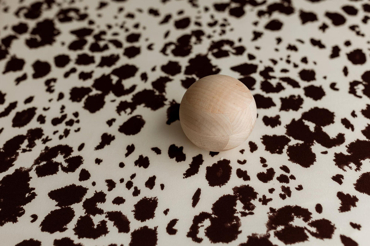 Frontier Days posing fabric with a cream and brown cow print pattern and a smooth wooden sphere prop.