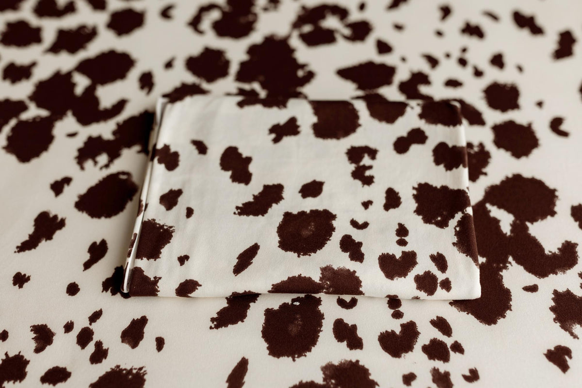 Soft, cream-colored posing fabric with a brown cow print pattern, folded neatly on a matching background.