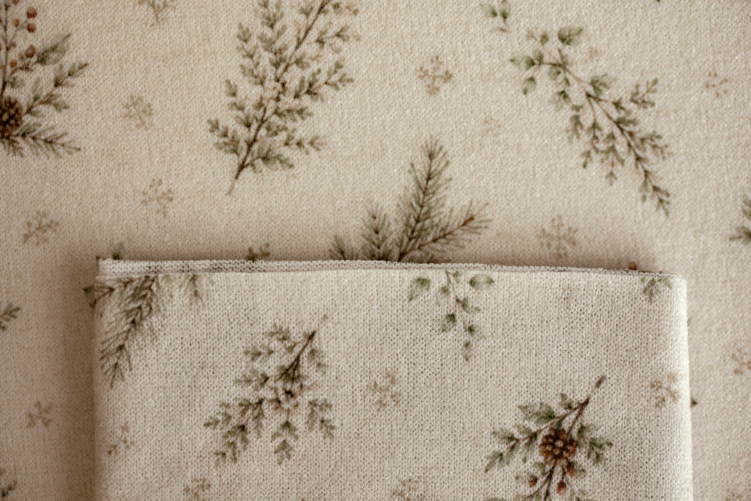Close-up of Mantle Garland cream newborn posing fabric and coordinating wrap featuring delicate evergreen branches and botanical details.
