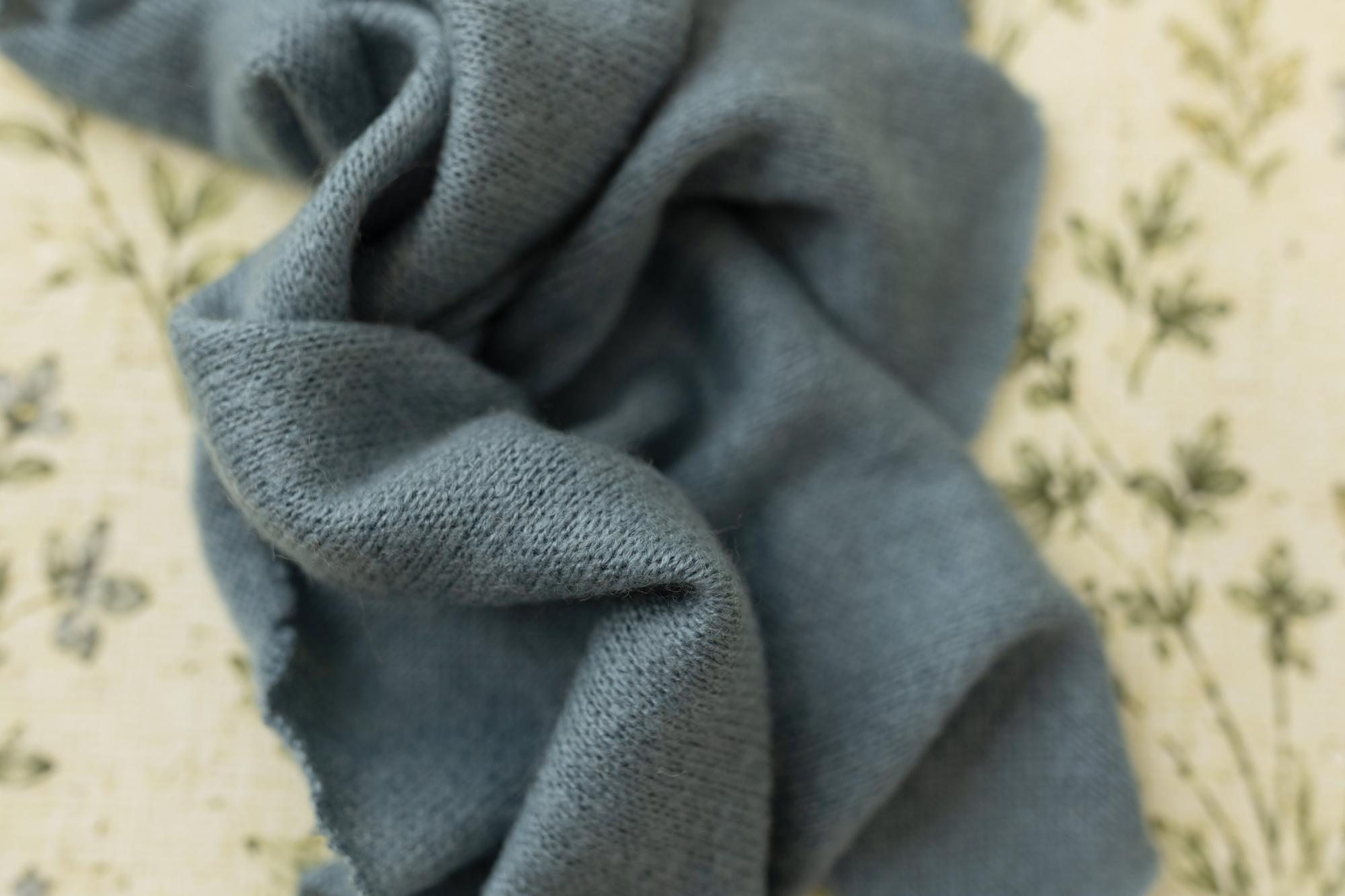 Soft, stretchy dusty blue fabric draped over a cream-colored floral posing backdrop for newborn photography.
