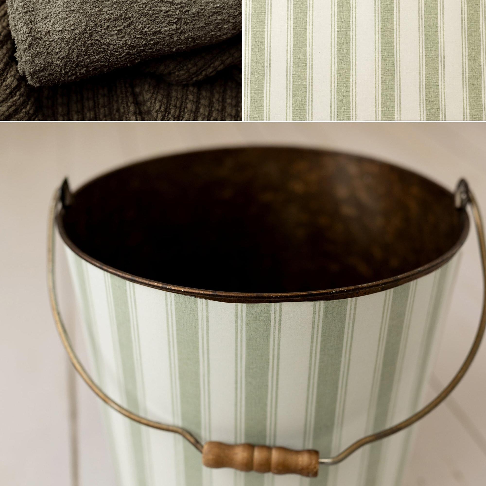 A vintage-style metal bucket with a pale green and white vertical stripe pattern, a dark metal interior, and a wire handle with a wooden grip. The image is a collage showing the bucket on a white wood floor, a close-up of the striped fabric, and a faded green Floof | Fir wrap.