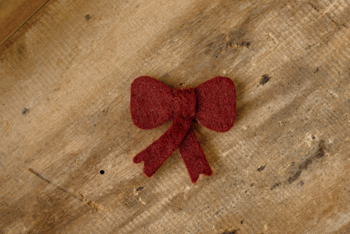 Deep red felted Christmas bow newborn photography lovie with ribbon tails, a sweet handheld prop for holiday newborn sessions.