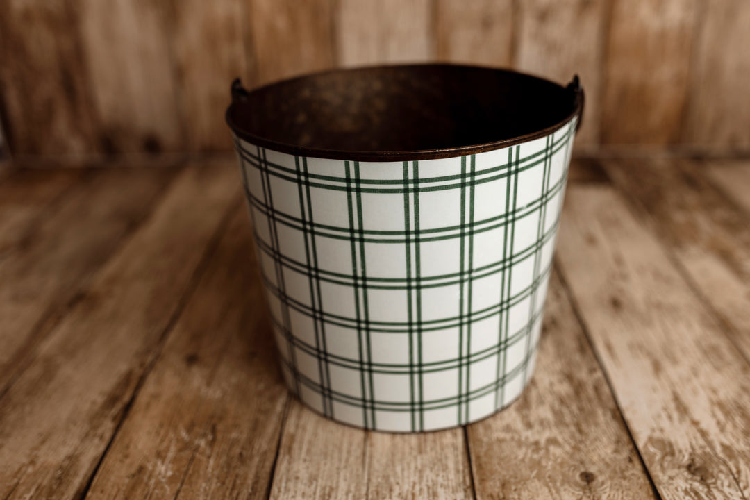 Product photo: Vintage metal newborn posing bucket wrapped in Under the Tree forest green plaid bucket cover, photographed on rustic wooden flooring.
