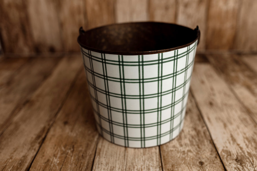 Product photo: Vintage metal newborn posing bucket wrapped in Under the Tree forest green plaid bucket cover, photographed on rustic wooden flooring.