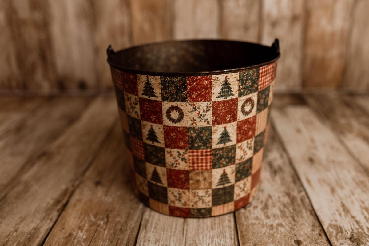 Very Merry Christmas bucket cover displayed on a rustic metal newborn posing bucket, featuring vintage red and green holiday patchwork with trees, wreaths, and plaid.