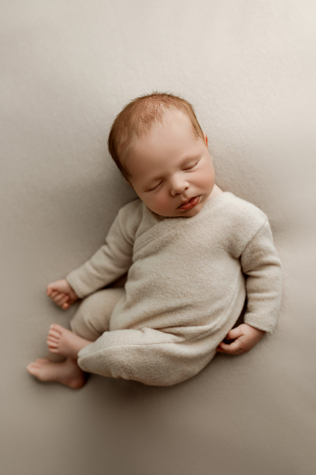Newborn wearing sand knit romper posed on matching photography fabric