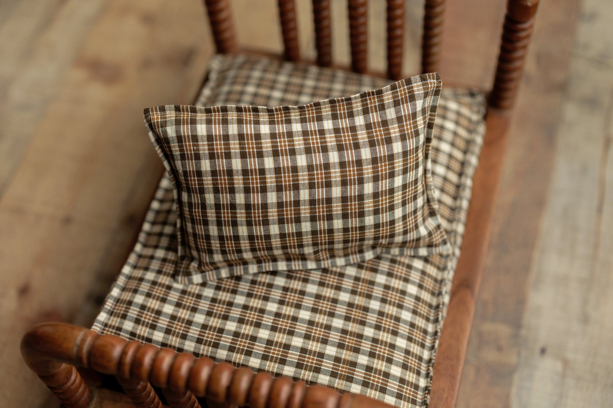 Newborn photography prop set featuring brown and cream plaid fabric sheets and a matching pillowcase on a wooden bed.