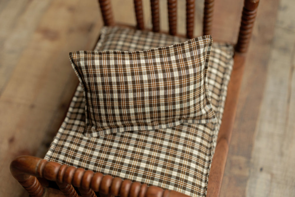Brown plaid newborn photography pillowcase displayed with matching sheets in a wooden prop bed, designed for rustic styled sessions.
