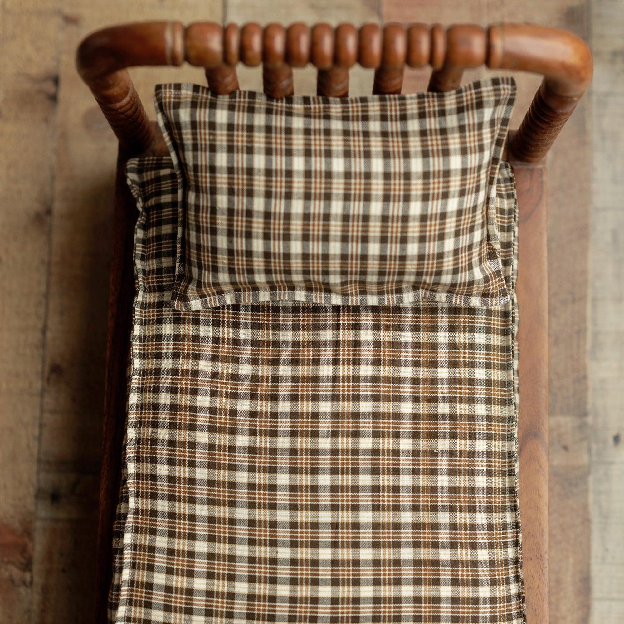 Brown plaid newborn photography sheet and pillowcase set on a rustic wooden bed prop.