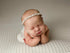 Newborn baby sleeping on off-white textured knit posing fabric with matching wrap and delicate floral headband.