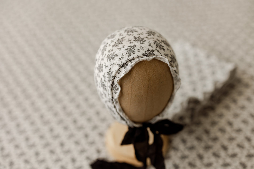 Ditzy floral newborn ruffle bonnet displayed on stand with coordinating fabric