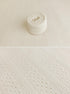 A close-up of a cream-colored knit fabric with a textured cable pattern, shown both as a rolled section and as a full fabric close-up.