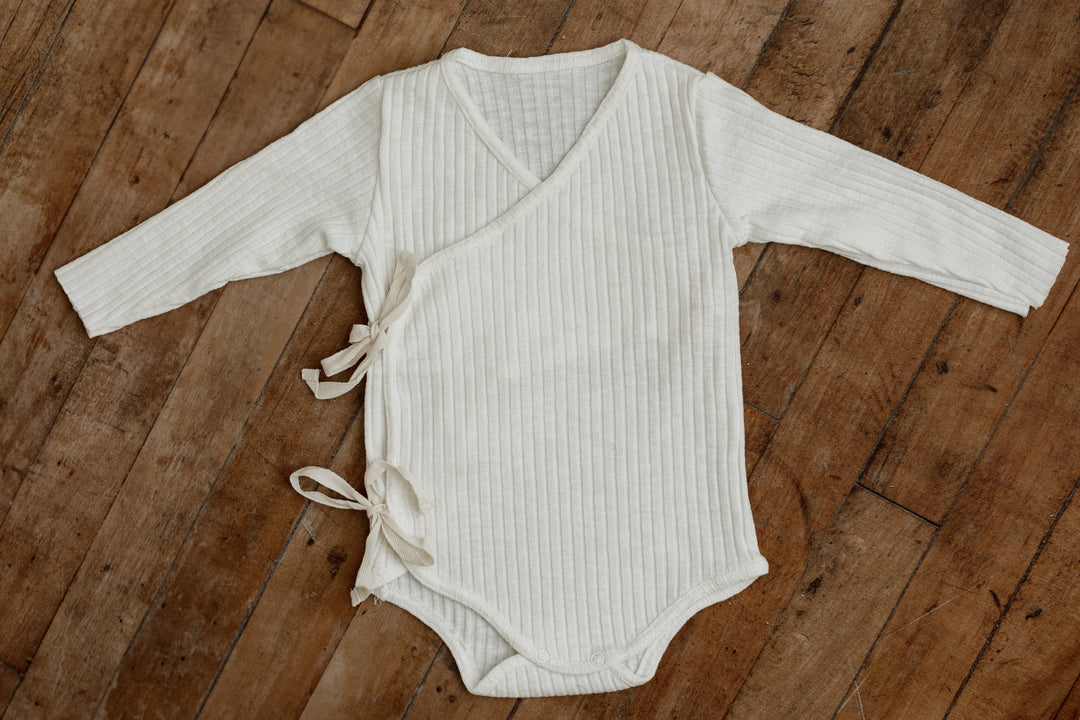 Ivory ribbed kimono-style sitter romper with side ties and long sleeves, designed for 6–12 month milestone photography sessions.