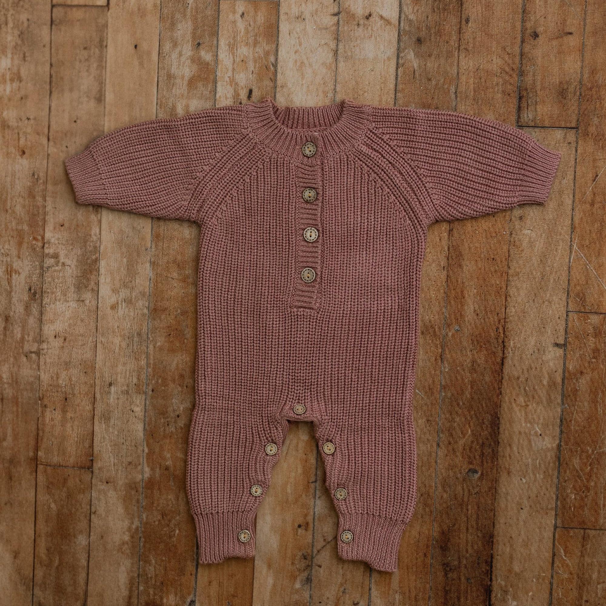 Plum knit sitter romper with button front, styled flat on wooden floor for milestone photography props.