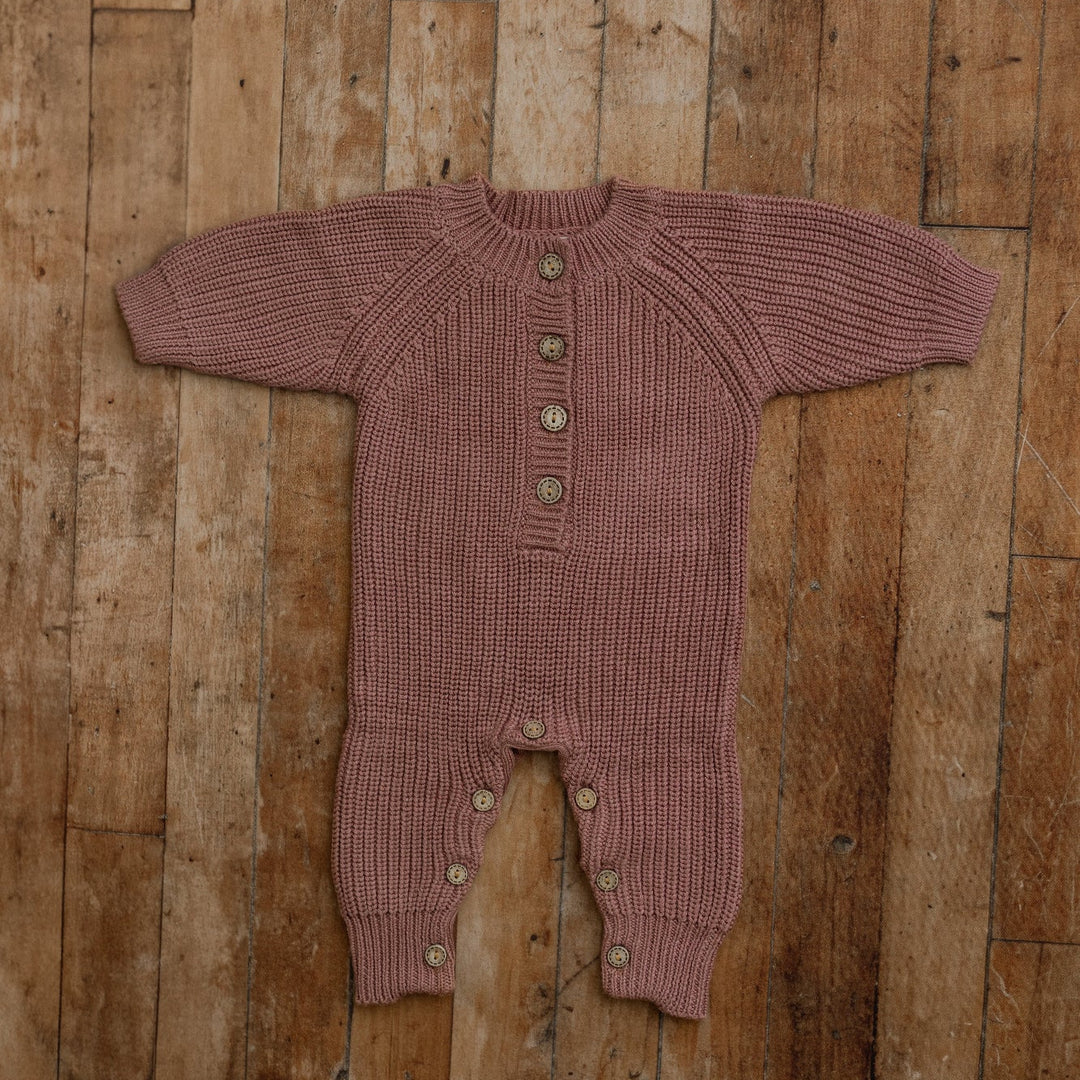 Plum knit sitter romper with button front, styled flat on wooden floor for milestone photography props.