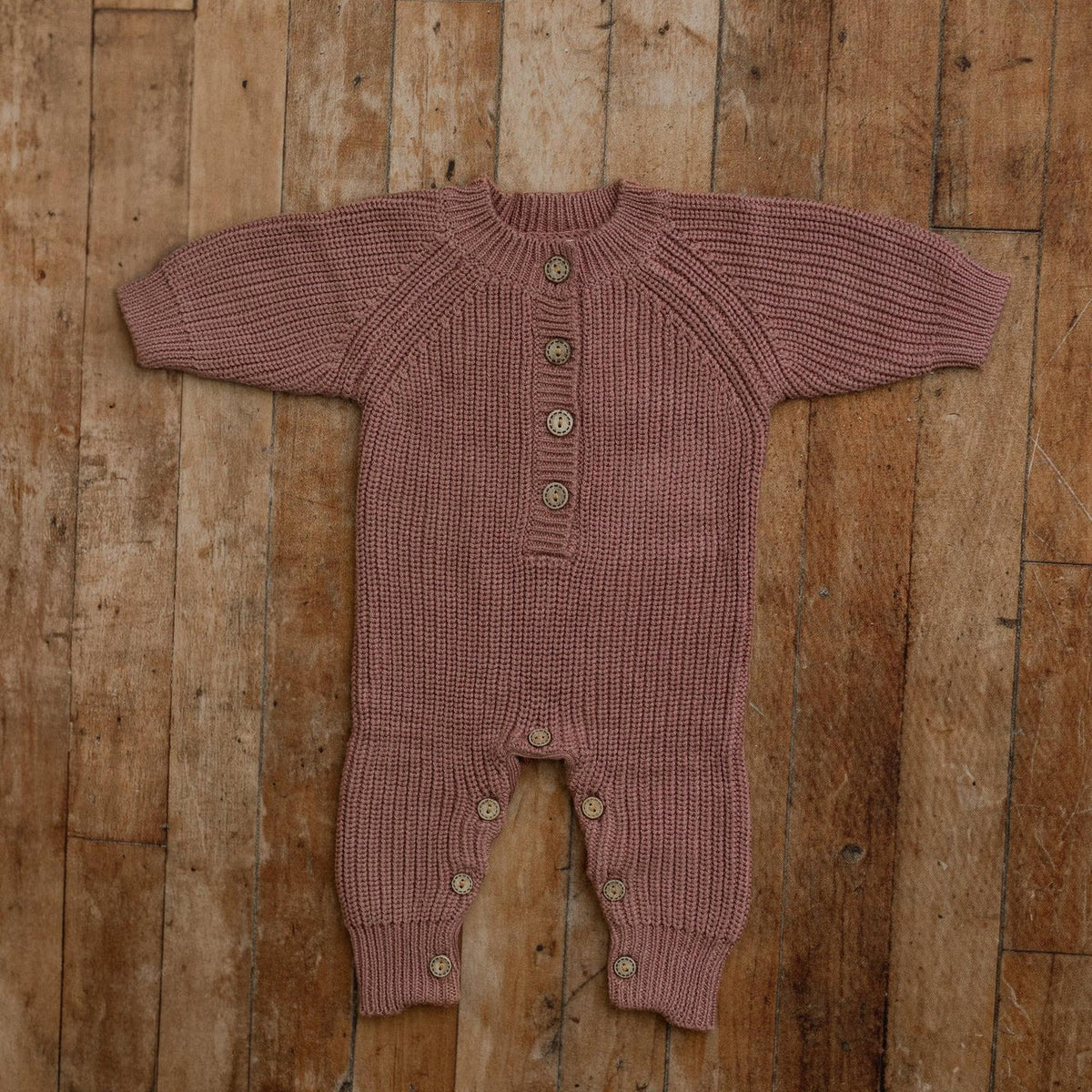 Plum knit sitter romper with button front, styled flat on wooden floor for milestone photography props.