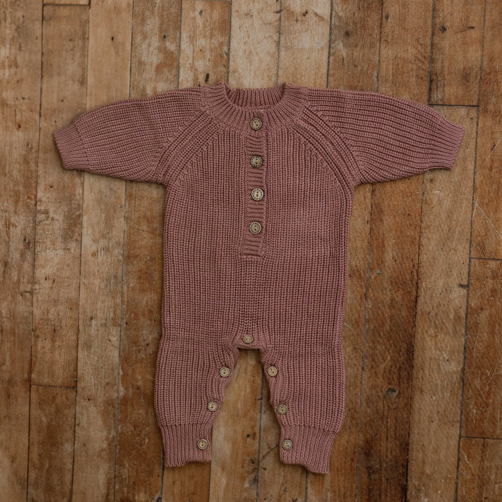 Plum knit sitter romper with button front, styled flat on wooden floor for milestone photography props.