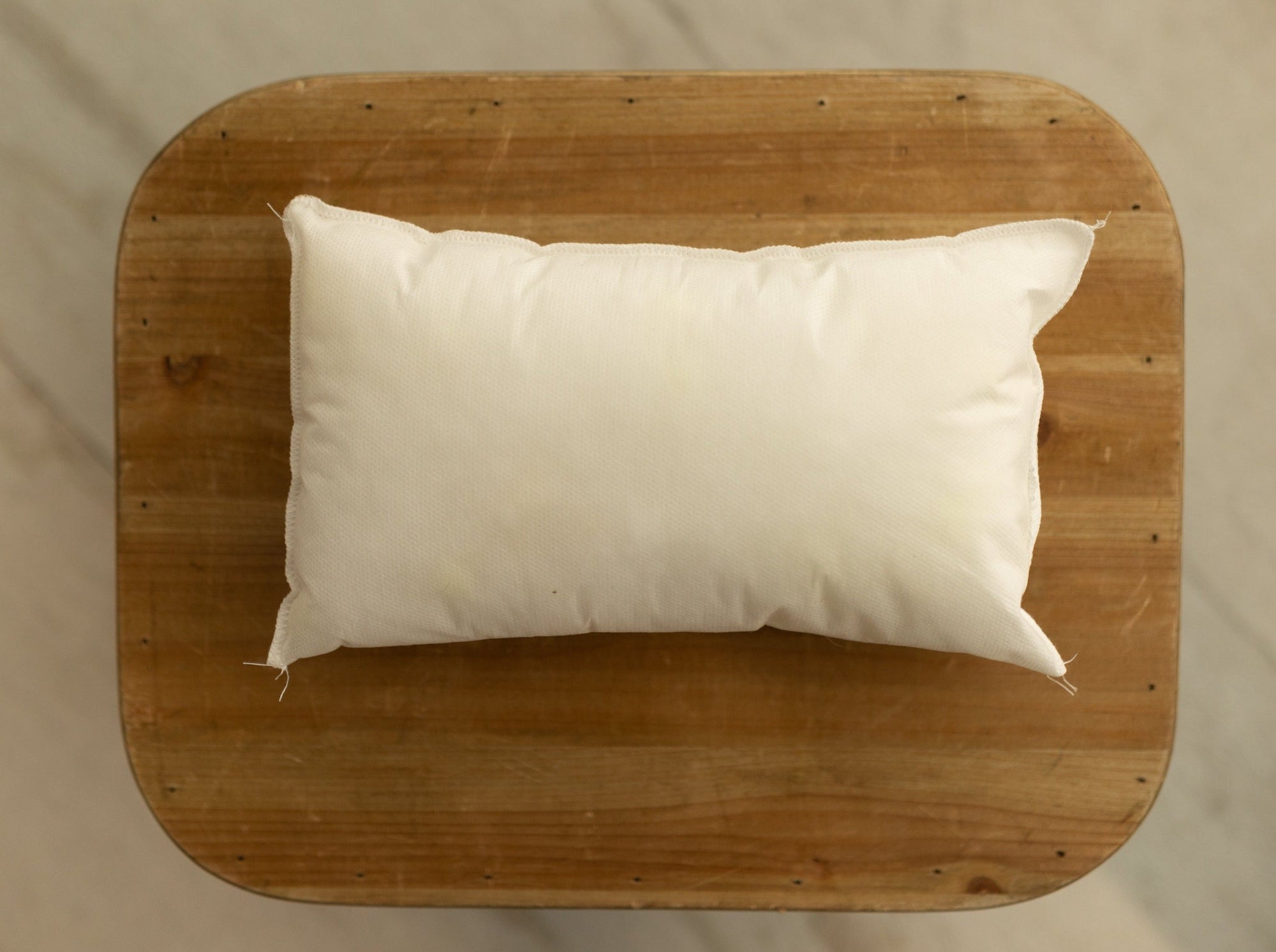Soft rectangular white newborn photography pillow insert resting on a rustic wooden surface.