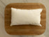 Soft rectangular white newborn photography pillow insert resting on a rustic wooden surface.