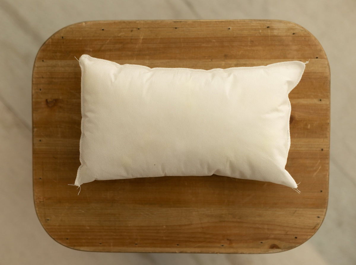 Soft rectangular white newborn photography pillow insert resting on a rustic wooden surface.
