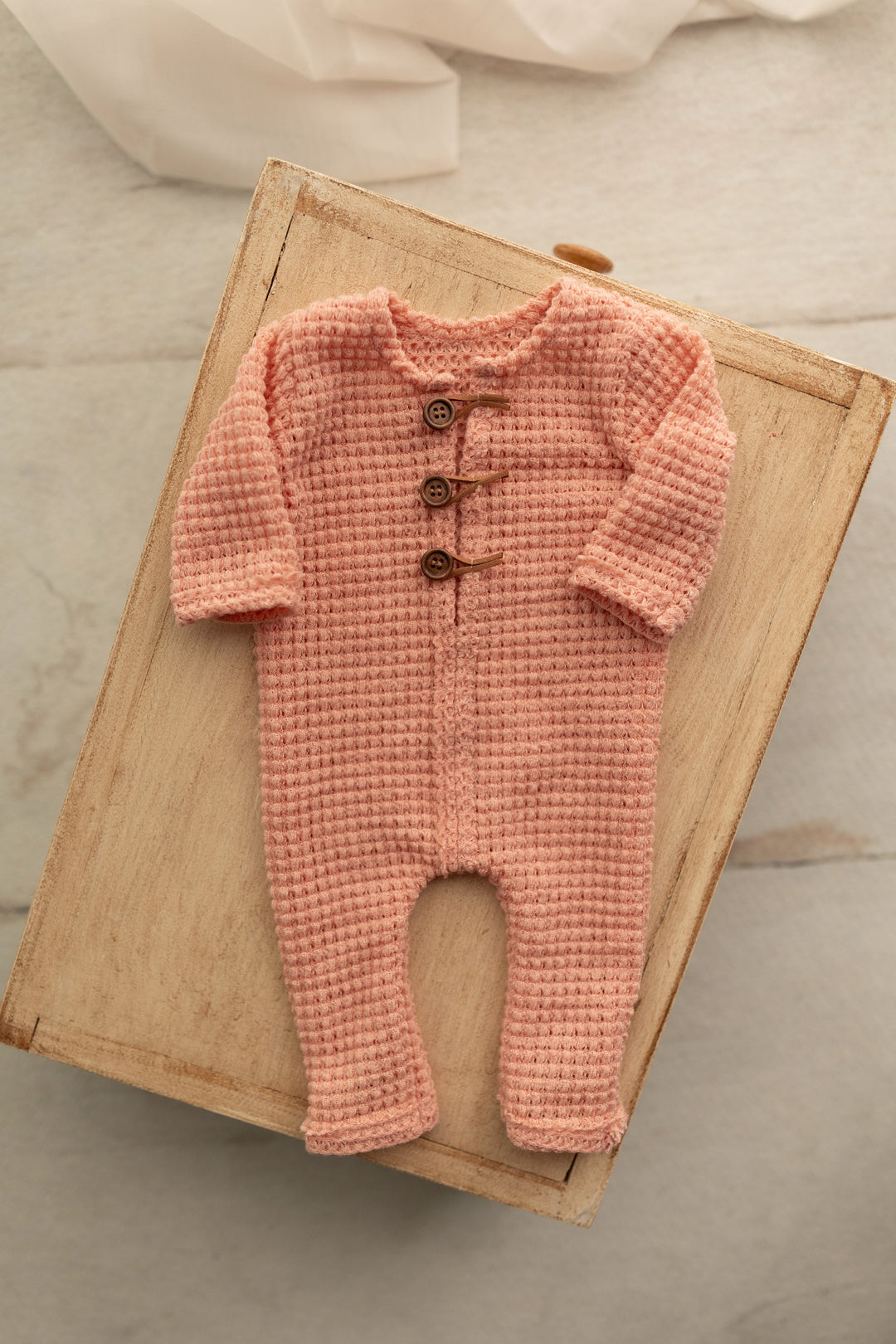 Peach knit newborn romper with wooden button details, styled flat on a wooden crate for photography use.