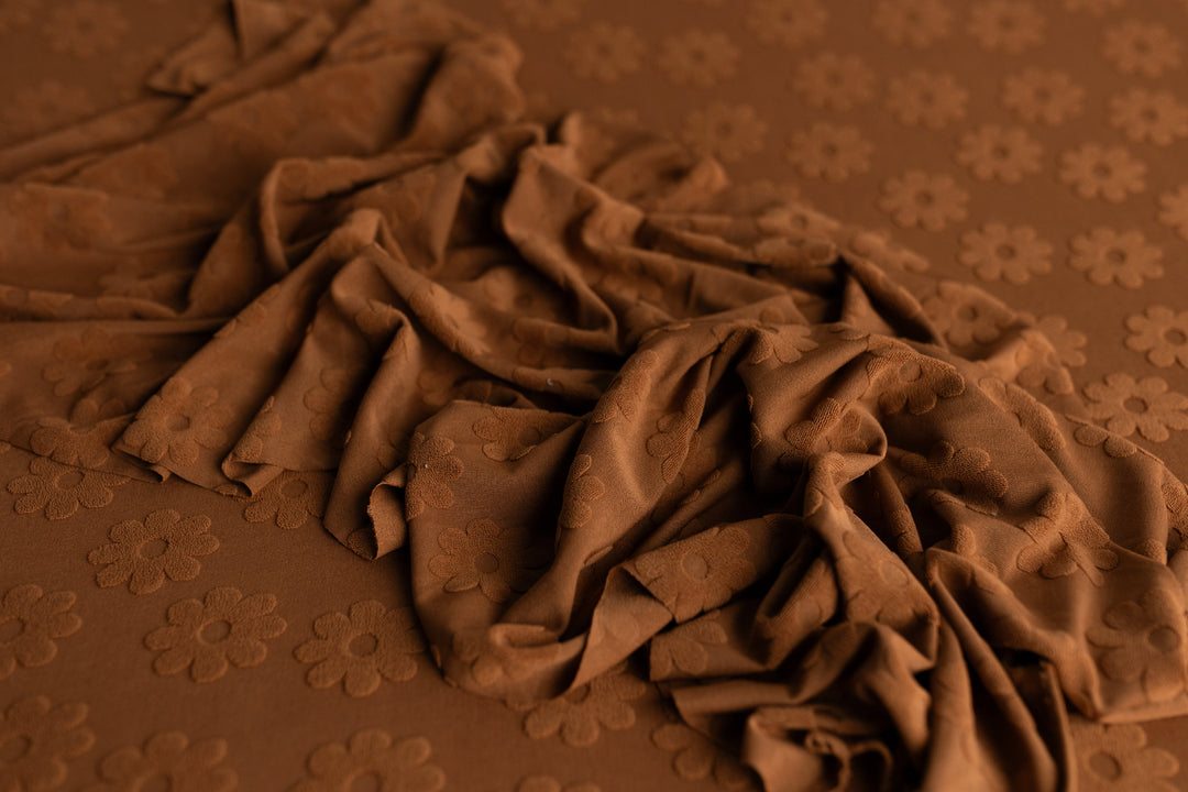 Rust daisy-patterned newborn wrap with raised floral texture, styled for layering in newborn photography sessions.