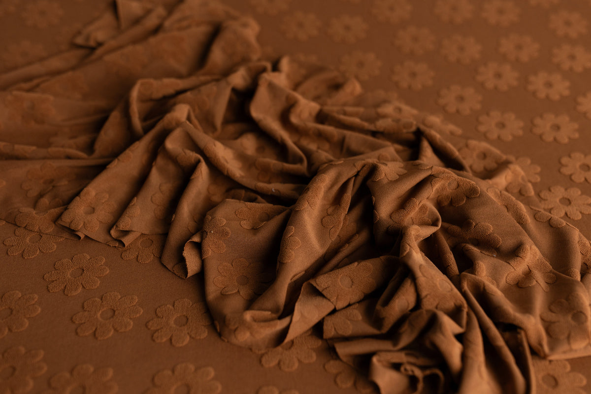 Rust daisy-patterned newborn wrap with raised floral texture, styled for layering in newborn photography sessions.