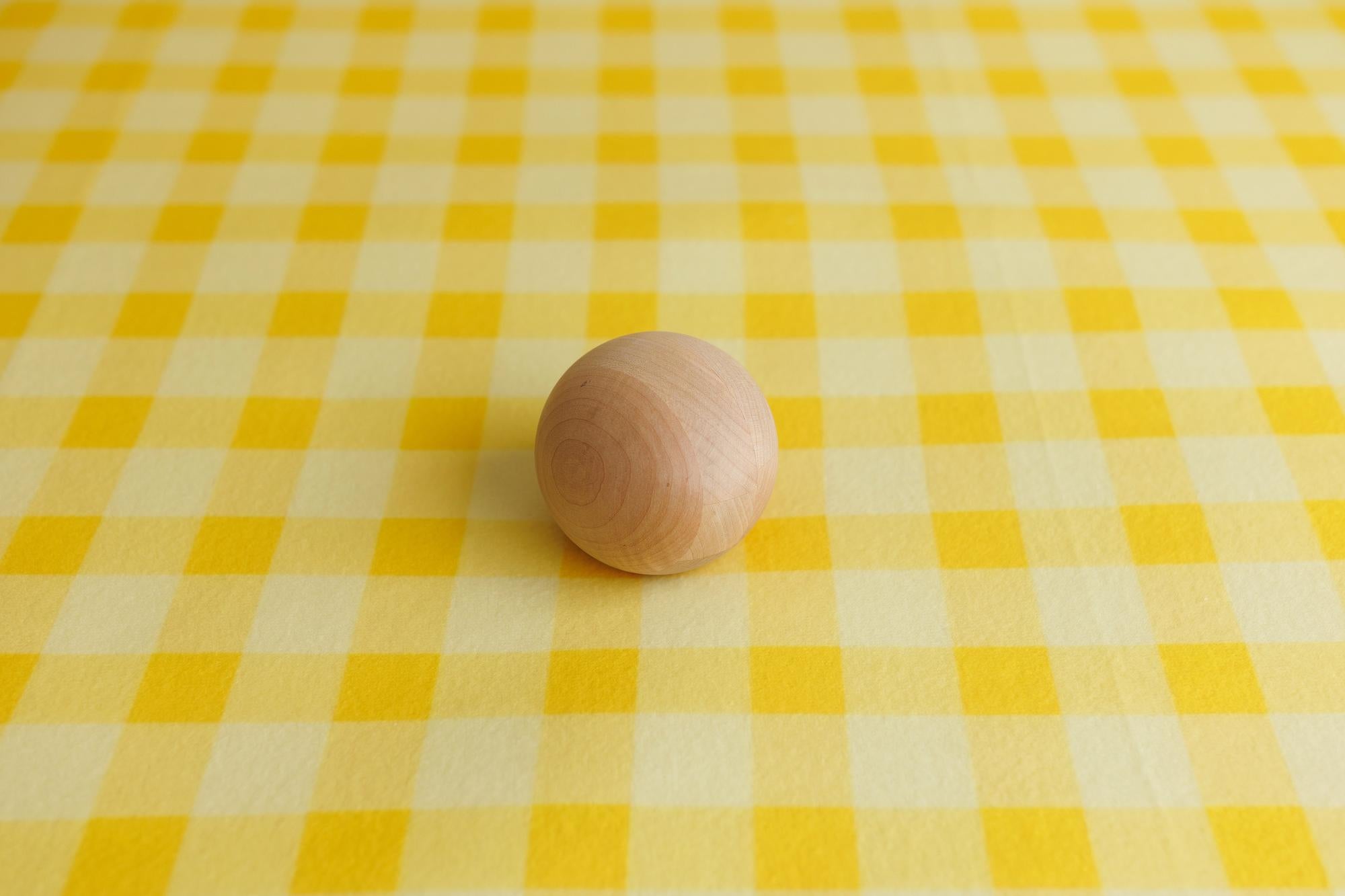 Soft buttery yellow and cream gingham photography fabric backdrop with a smooth wooden sphere prop.