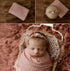 Soft pink strawberry milk newborn photography wrap with a textured, open-knit design and matching floral tieback.