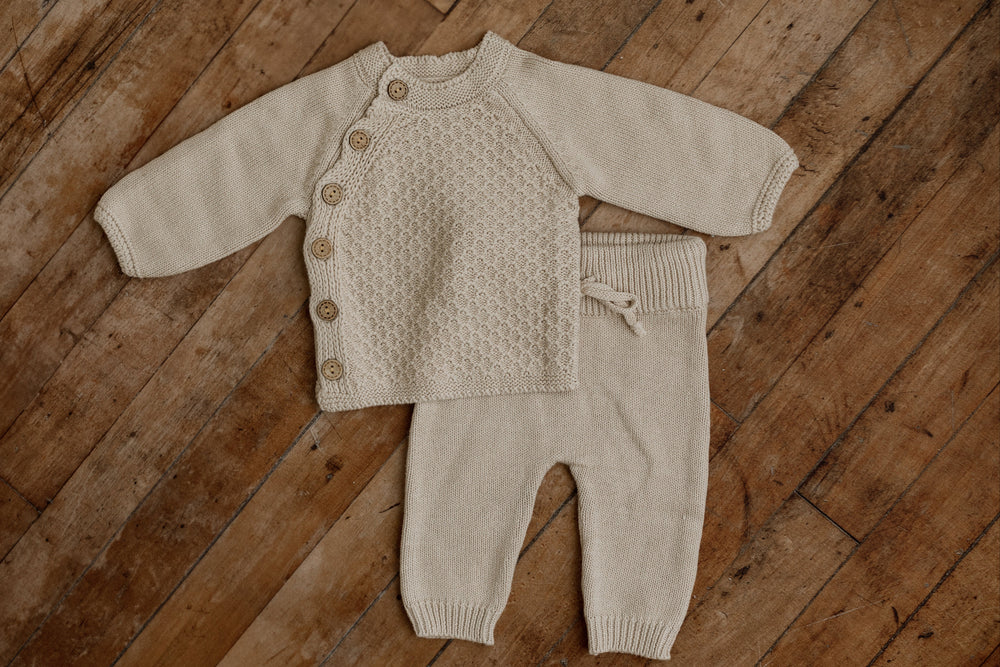 Woodland newborn knit set with cable-knit button cardigan and matching shorts in taupe beige, displayed flat on wooden floor for photography props.